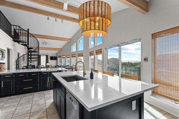 A spacious kitchen with a central island, a spiral staircase, and large windows offering a view of the outdoors.