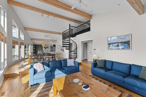 A spacious living room with a large blue sofa, a wooden coffee table, and a staircase leading to an upper level.