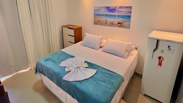 Ein Hotelzimmer mit Bett, Nachttisch, Kühlschrank und einem Gemälde an der Wand.