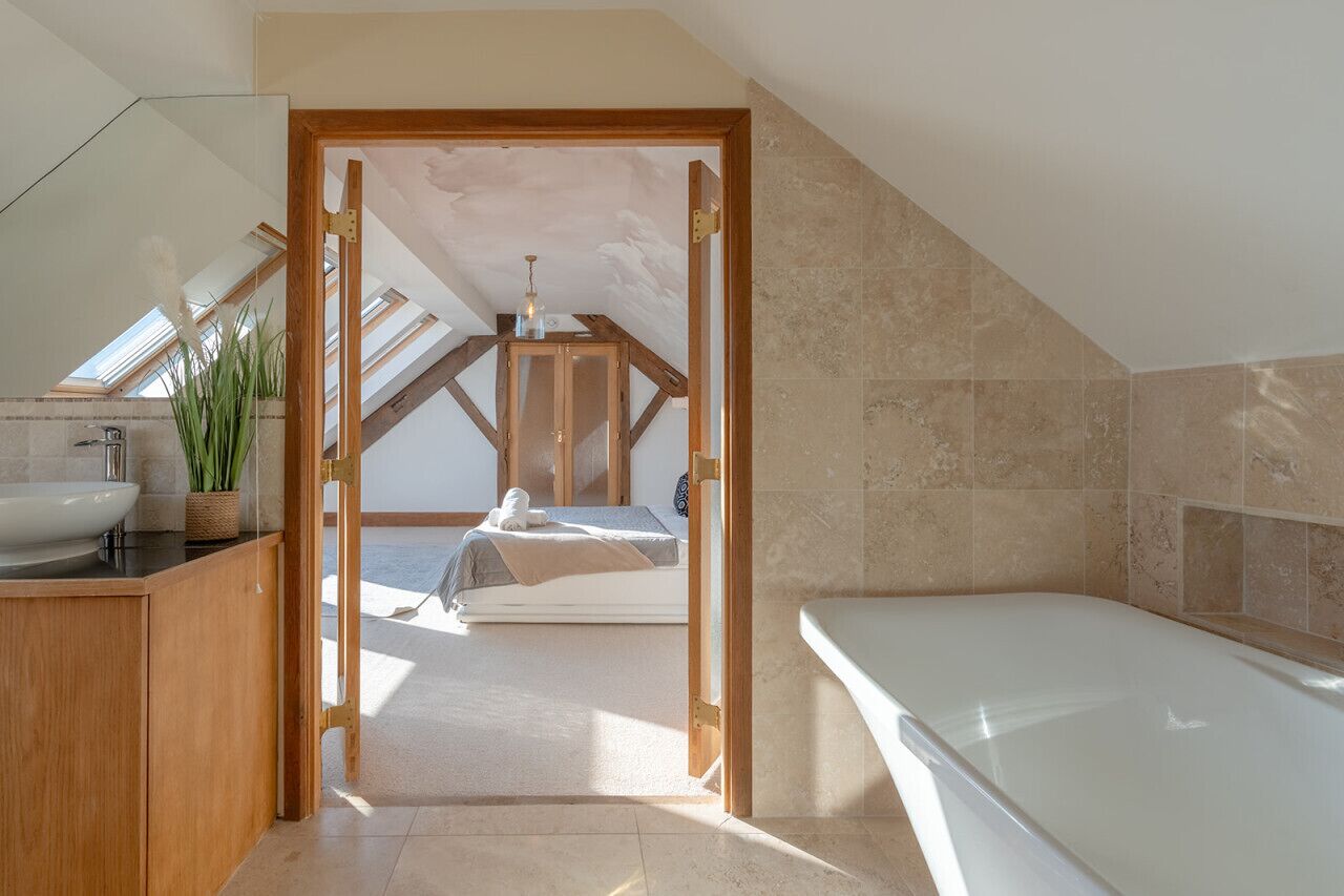 Un dormitorio moderno con tragaluces, un ventanal grande, techo de madera, una cama, una mesita de noche y un baño con bañera.