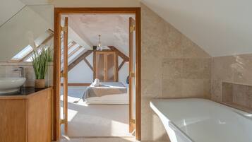 Un dormitorio moderno con tragaluces, un ventanal grande, techo de madera, una cama, una mesita de noche y un baño con bañera.