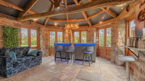Ein rustikales Interieur mit Steinwänden, Holzbalkendecke, einer Bar mit Hockern und einem Sofa.