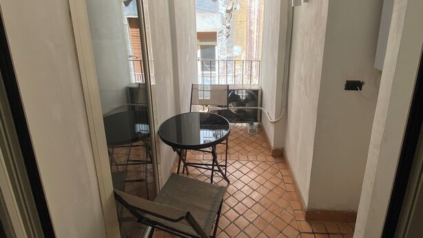 A small, enclosed balcony with a table and chairs, a window with a view, and a tiled floor. - Dimora Tribunali 236, main street, 300 mt from metro (Napoli)