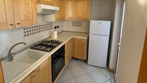 A compact kitchen with wooden cabinets, a gas stove, a sink, and a white refrigerator. - Dimora Tribunali 236, main street, 300 mt from metro (Napoli)