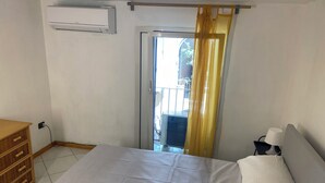 A bedroom with a bed, a wooden dresser, an air conditioning unit, a nightstand with a lamp, and a sliding glass door leading to an outdoor area. - Dimora Tribunali 236, main street, 300 mt from metro (Napoli)