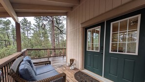 A wooden deck with a wicker sofa and a bench, a green door, and a view of trees. - HIDDEN SPACIOUS 4-bdr RETREAT FOR FAMILIES AND FRIENDS!  (Show Low)