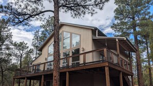 A two-story cabin with a wooden deck and large windows, surrounded by trees. - HIDDEN SPACIOUS 4-bdr RETREAT FOR FAMILIES AND FRIENDS!  (Show Low)