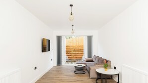 Una sala moderna con piso de madera, una mesa de centro redonda, un sofá y vista a una terraza de madera a través de puertas de vidrio.