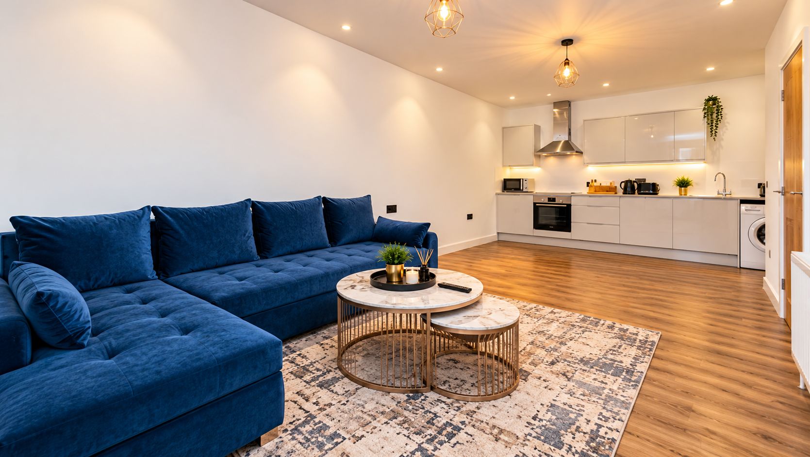 Ein modernes Wohnzimmer mit einem blauen Ecksofa, zwei runden Couchtischen und einer Küche im Hintergrund.
