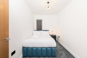 Un dormitorio con cama, mesita de noche y ventana.