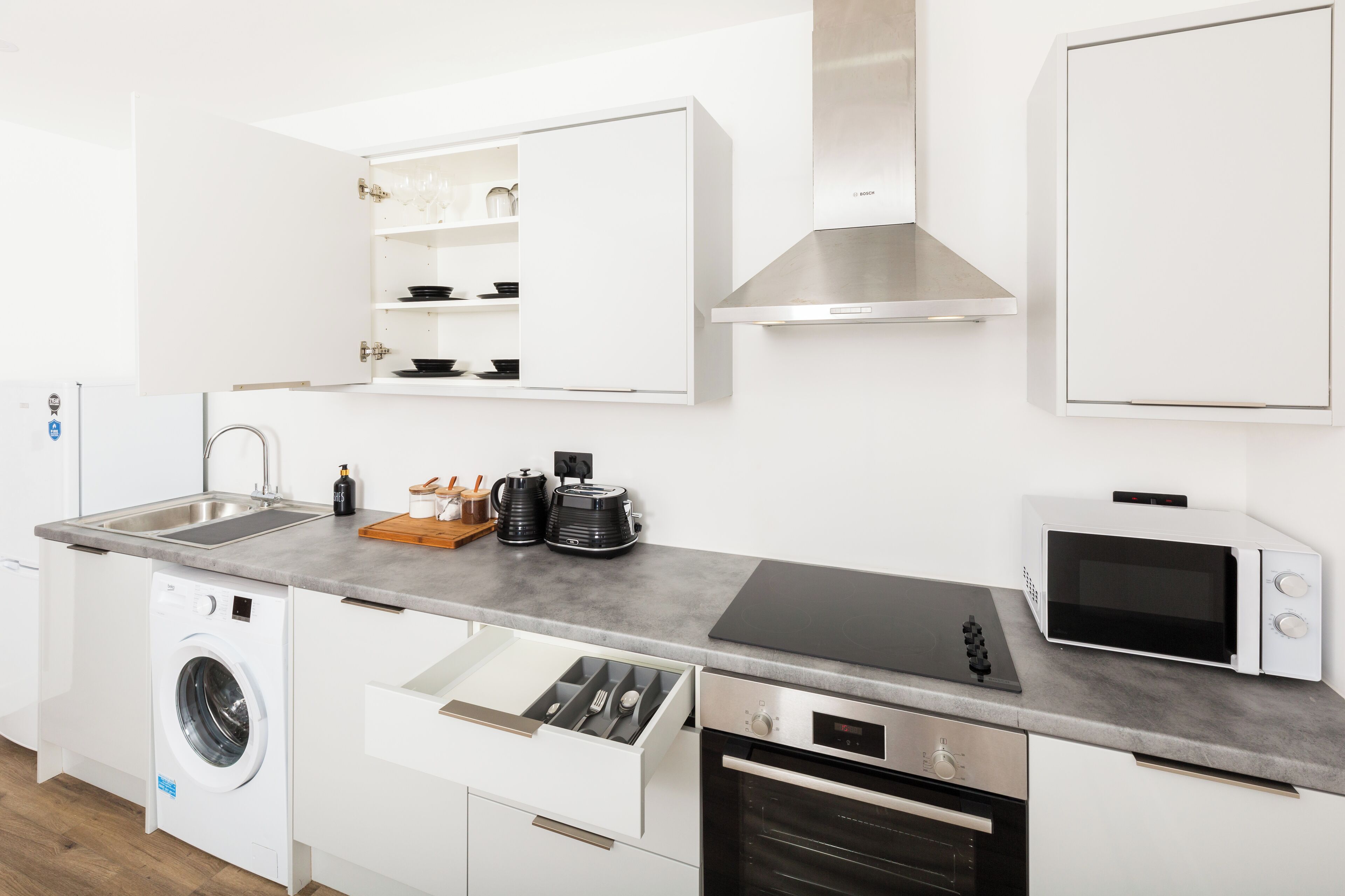 Una cocina moderna con lavadora integrada, microondas, estufa y lavabo.