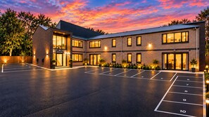 A hotel with a reception area, multiple parking spaces, and a well-lit exterior.