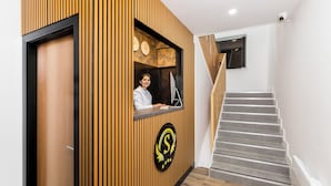 Un mostrador de recepción con diseño de paneles de madera, un logotipo y una escalera con alfombra gris.