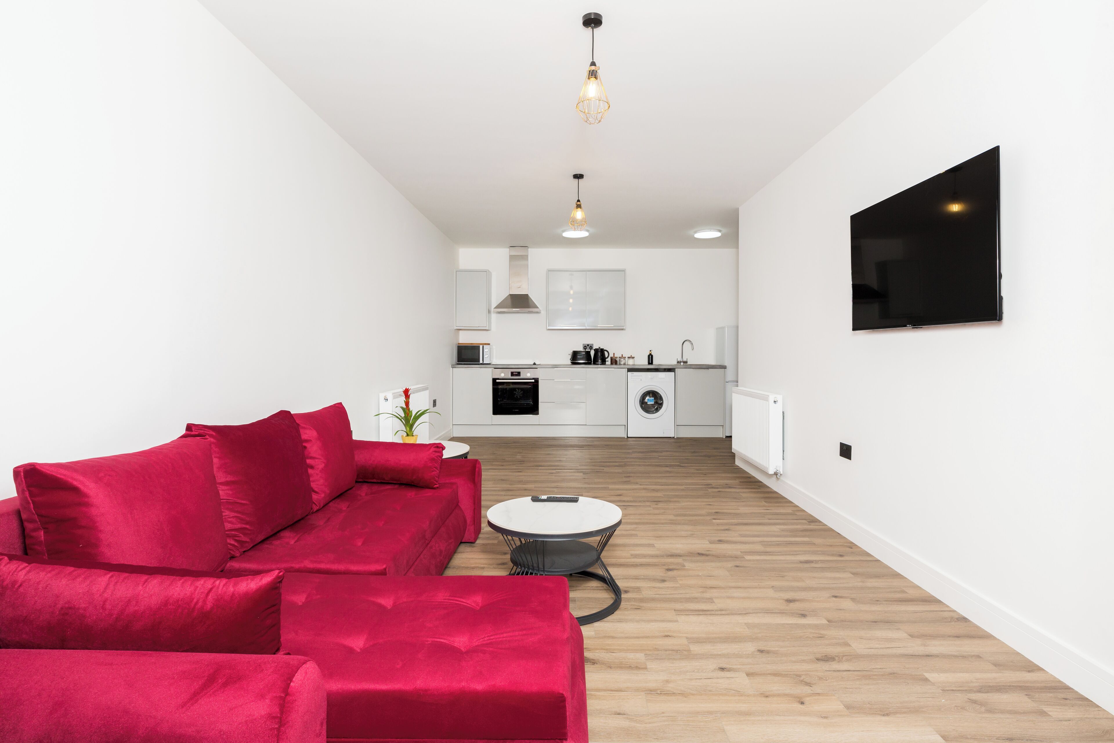 A modern living room with a red sofa, a round coffee table, and a kitchen in the background.
