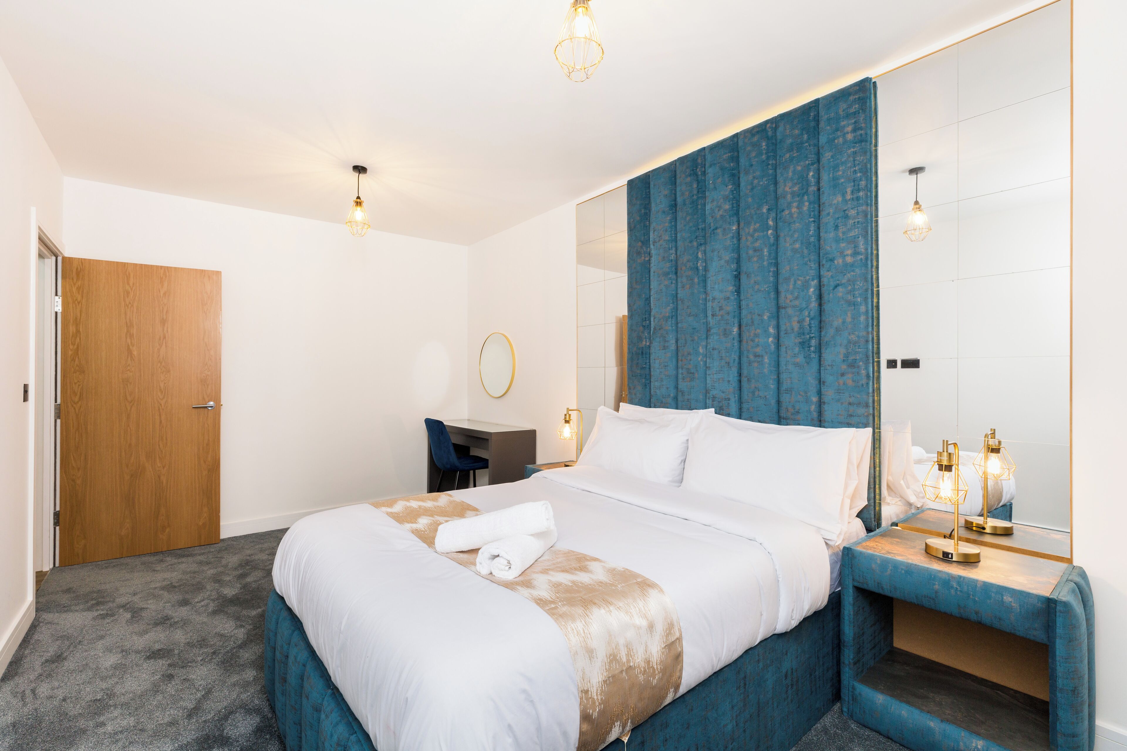 A modern hotel room with a large bed, a desk, a chair, and a bathroom mirror.