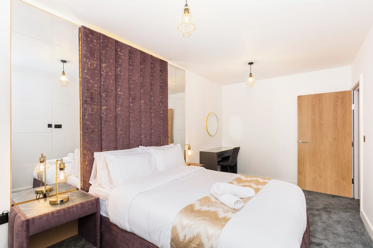Une chambre d’hôtel avec un grand lit, un bureau, un miroir et une porte en bois.