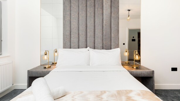 Un dormitorio de hotel moderno con una cama grande, un cabecero gris y lámparas de noche.