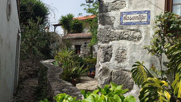 Ein schmaler Steinweg führt zu einem Gebäude, an dem ein Schild mit der Aufschrift "Casantiga" hängt.