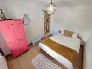 Ein Schlafzimmer mit einem Bett, einem pinken Kleiderschrank, einem Nachttisch, einer Pendelleuchte und einem an der Wand befestigten Spiegel.