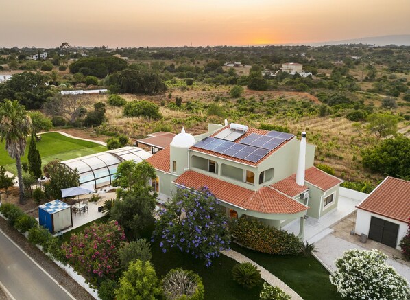 Een huis met een dakbedekt met zonnepanelen, een zwembad en een tuin met diverse planten en bloemen.