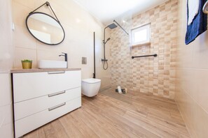 A modern bathroom with a white vanity, a round mirror, a glass-enclosed shower, and a tiled floor. - Villa Las Salinas (Silves)