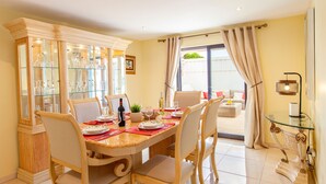 A dining area with a glass cabinet, dining table set with plates and glasses, and a view to a balcony. - Villa Thai (Albufeira)