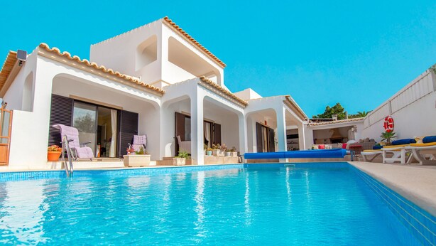 A swimming pool with a clear blue water, surrounded by white buildings with balconies and windows. - Villa Thai (Albufeira)