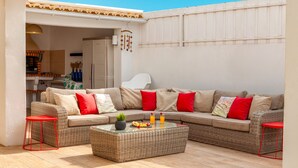 A cozy outdoor seating area with a wicker sofa, red cushions, and a glass-top coffee table. - Villa Thai (Albufeira)
