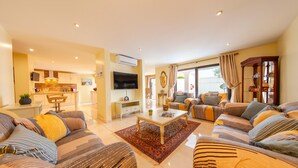 A modern living room with a sofa set, a coffee table, and a TV. There is a kitchen area in the background. - Villa Thai (Albufeira)