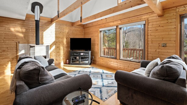 A cozy cabin interior with a wooden interior, a fireplace, a television, and a large window offering a view of the outdoors.