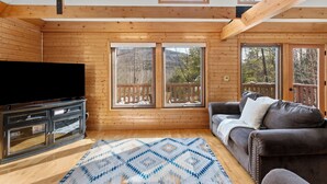 A cozy cabin interior with wooden walls, a large TV, a sofa, and a patterned rug.