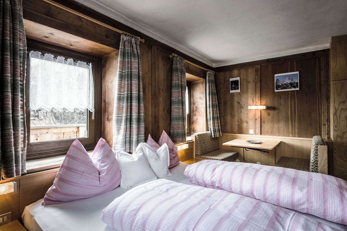 A cozy room with a bed, a desk, and a chair. There are curtains on the windows, and a picture on the wall.