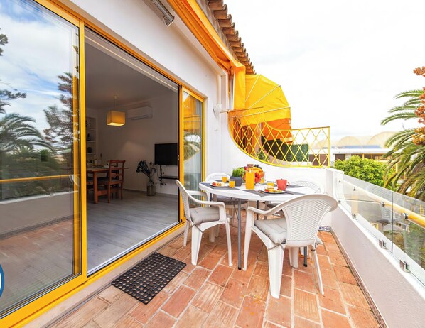 A balcony with a table and chairs, a yellow umbrella, and a view of the surrounding landscape. - Apartment Portofino 2 (Loulé)