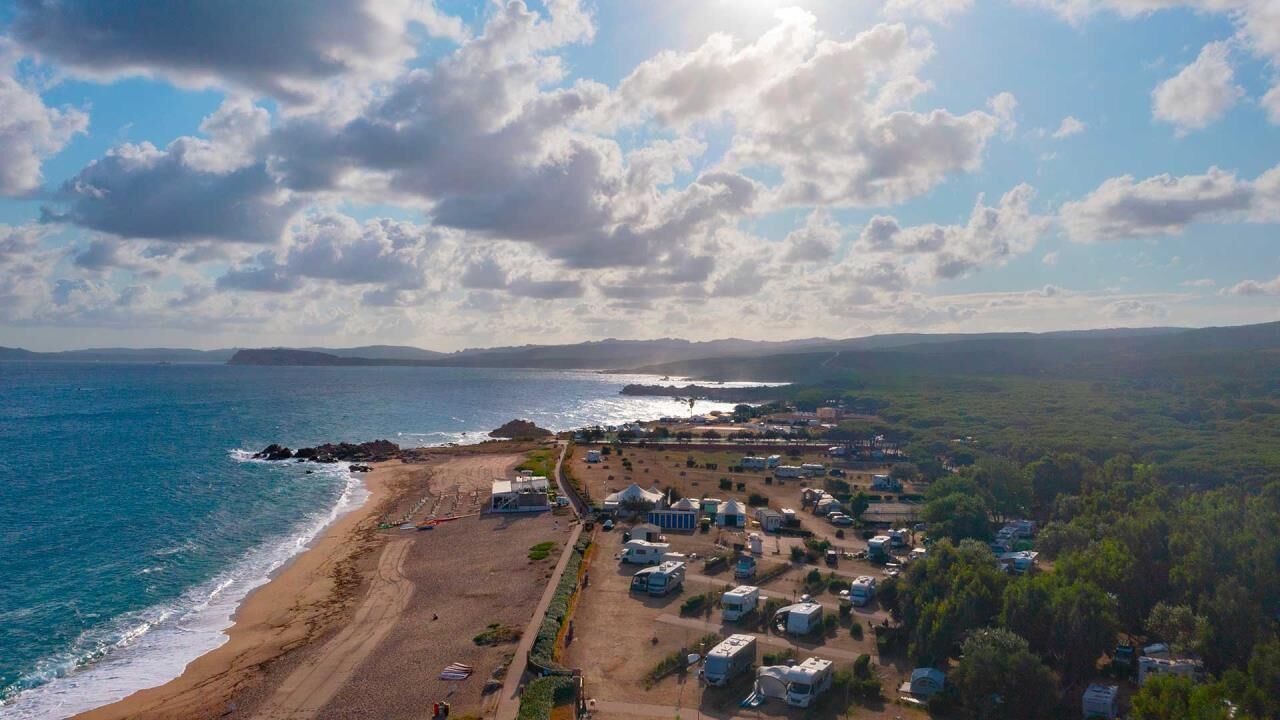 An aerial view of a coastal area with a beach, RVs, and a distant island.