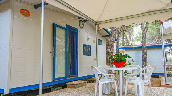 A mobile home with a covered patio area, white plastic chairs, and a potted plant.