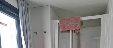 Pieni kylpyhuone, jossa on wc, suihkukaappi ja ikkuna, jossa on verhot.