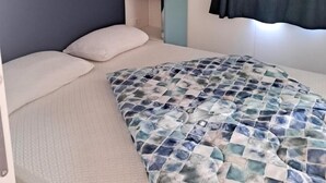 Ein kleines Zimmer mit Etagenbett, einem kleinen Nachttisch, einem Einzelbett mit gemustertem Überwurf und einem Fenster mit Verdunkelungsvorhängen.