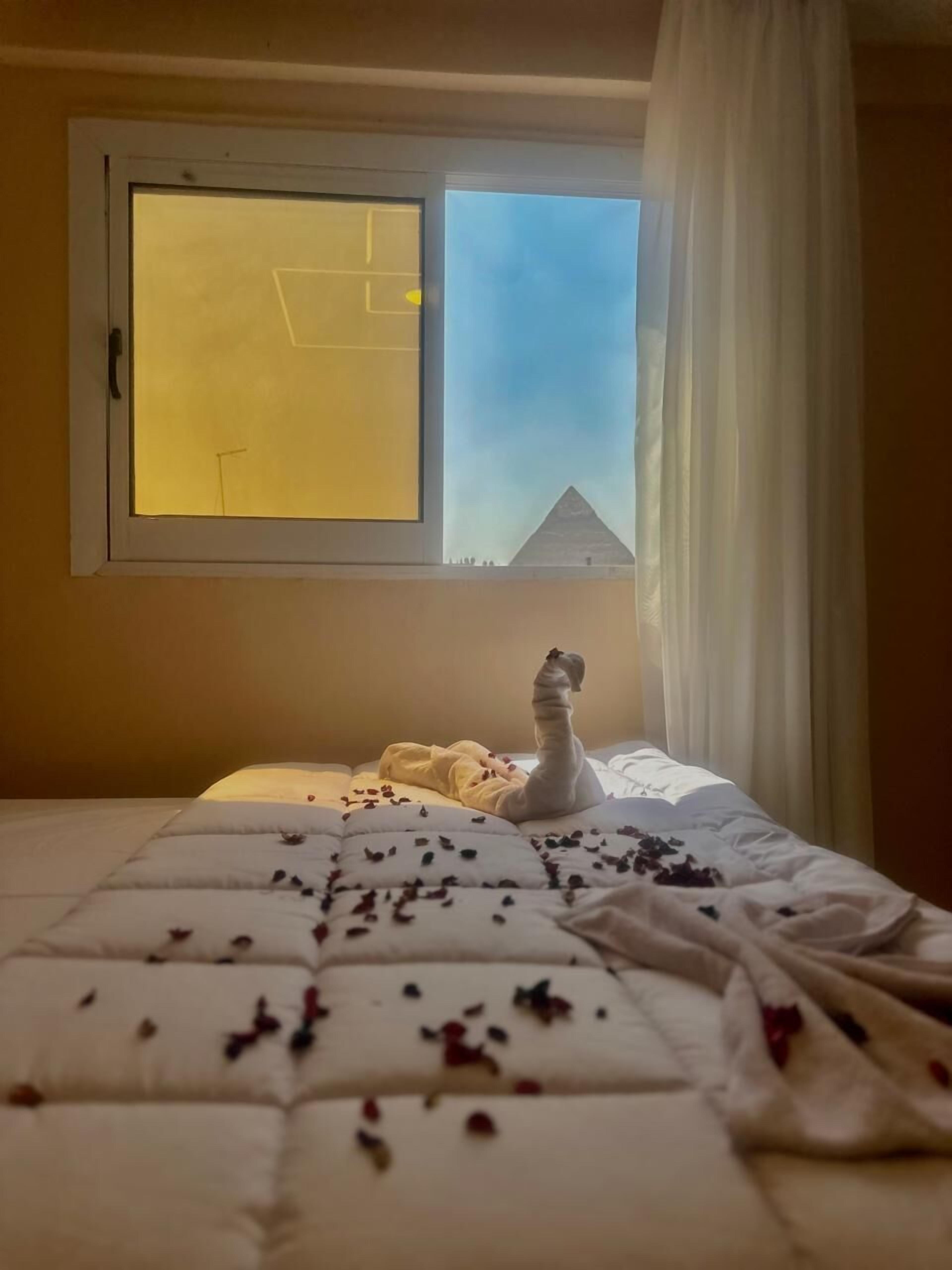A bedroom with a bed, a window with a view of a pyramid, and a swan decoration on the bed.
