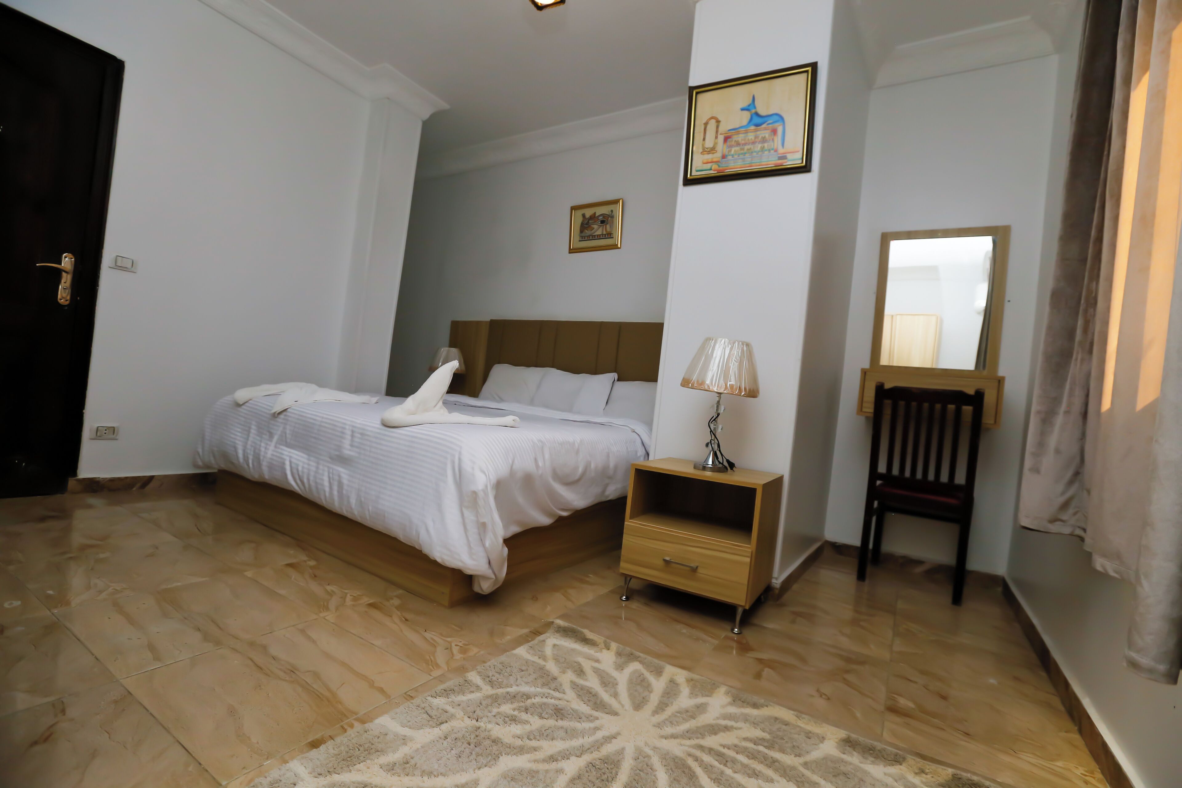 A bedroom with a bed, bedside table, lamp, chair, and a rug.