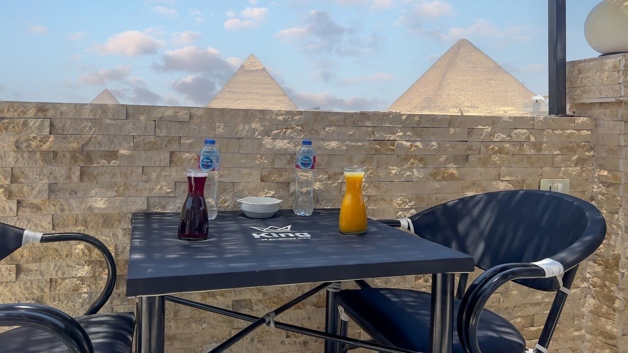 A table with drinks and a logo, set against a stone wall with pyramids in the background.