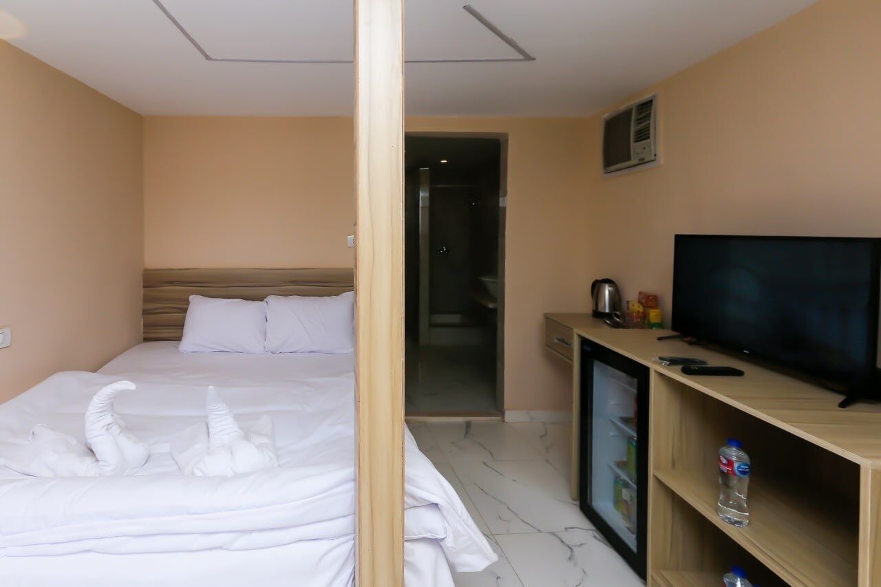 A hotel room with a bed, a television, a minibar, and a bathroom visible through an open door.
