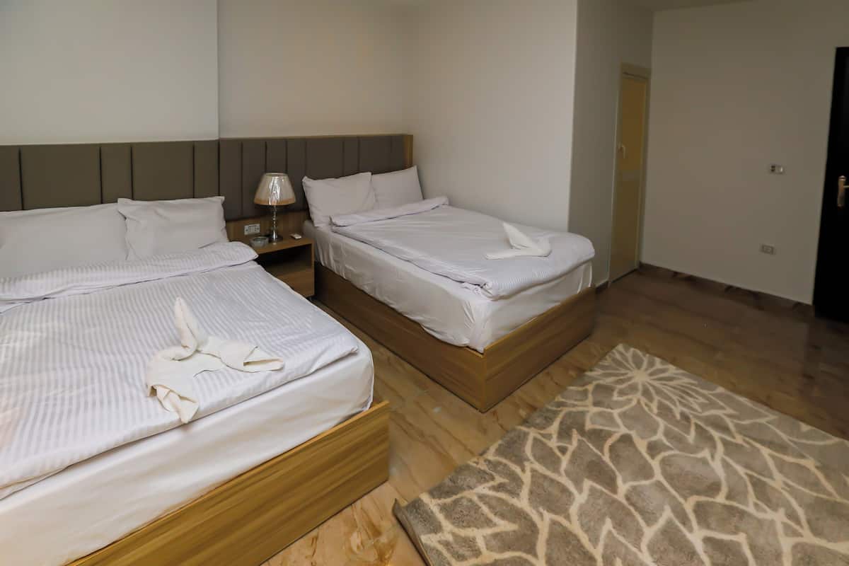 A hotel room with two beds, a nightstand with a lamp, and a patterned rug.