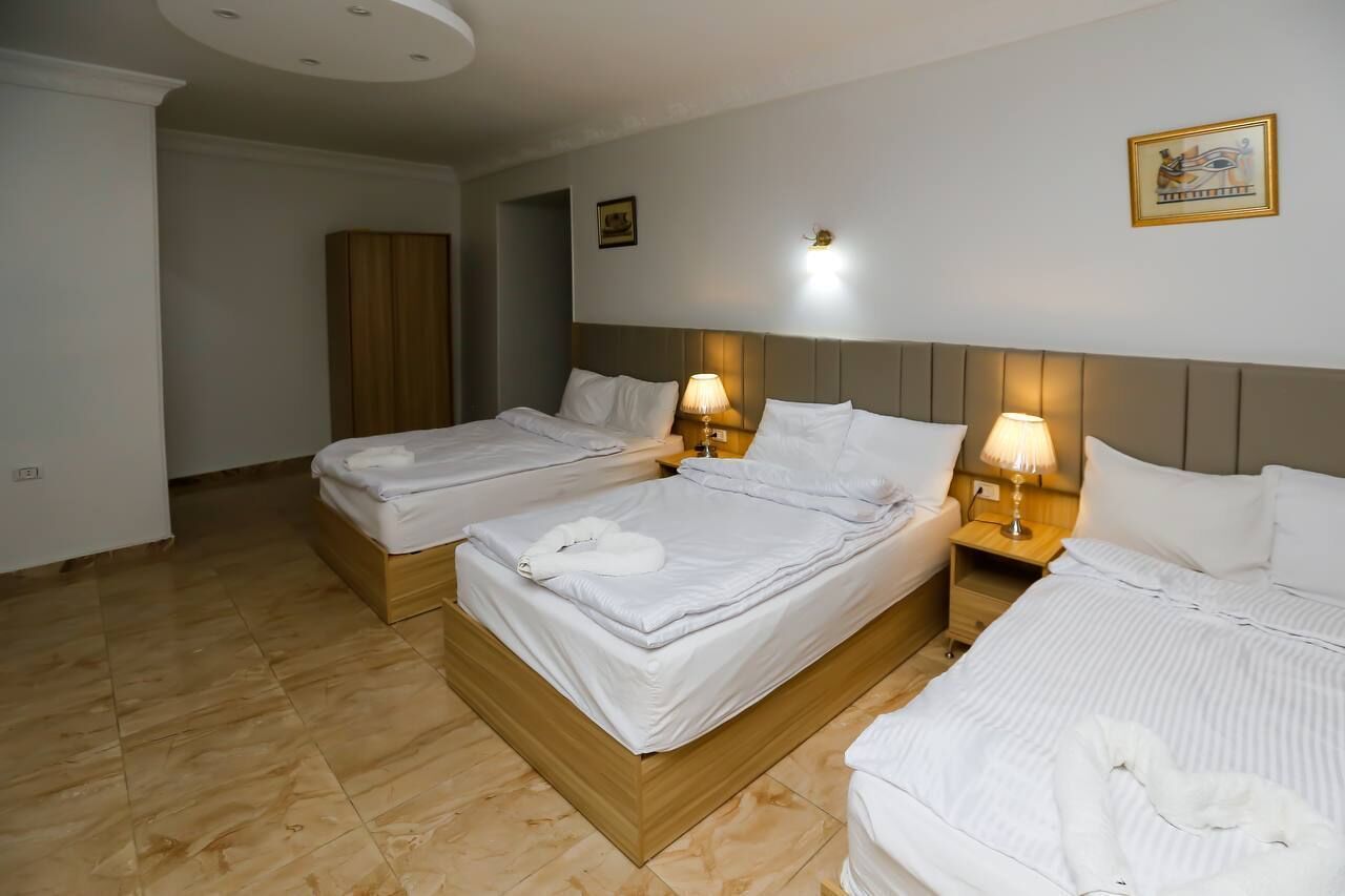 A hotel room with two beds, each with white linens and pillows, a wooden headboard, and bedside lamps.