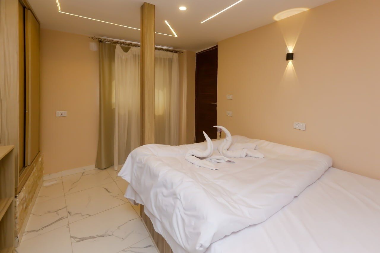 Ein Hotelzimmer mit einem großen Bett, einem Spiegel, einer Wandleuchte und einem Vorhang.