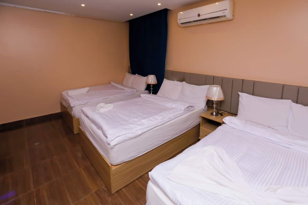 A hotel room with two beds, a wooden headboard, a nightstand with a lamp, and an air conditioning unit on the wall.