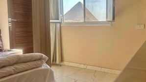 A bedroom with a bed, a window with a view of pyramids, and a wooden door. -  Pyramids Express View Inn  (Giza)