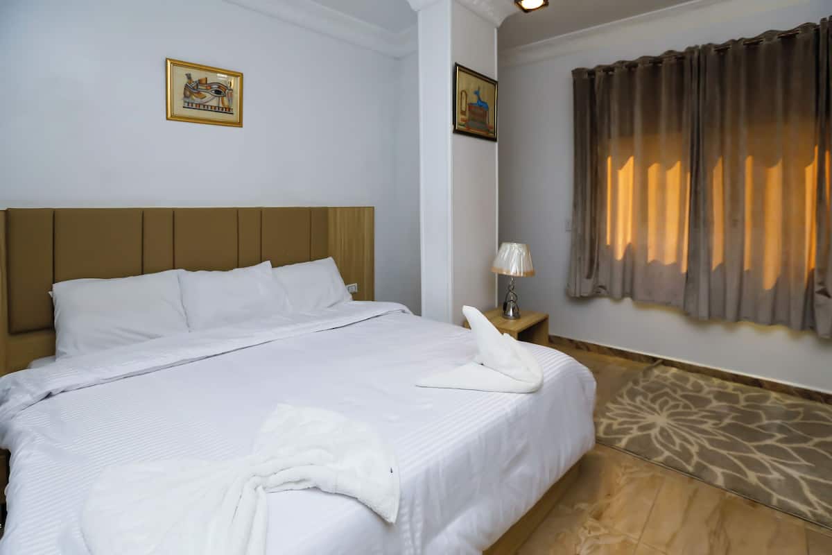 A neatly made bed with white linens and pillows, a bedside lamp, and two framed pictures on the wall.