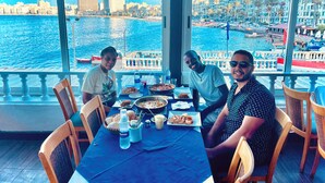 A dining area with a table set for four, overlooking a waterfront with buildings and boats. -  Pyramids Express View Inn  (Giza)