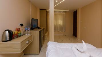 A hotel room with a bed, a desk with a kettle, a TV, and a minibar.