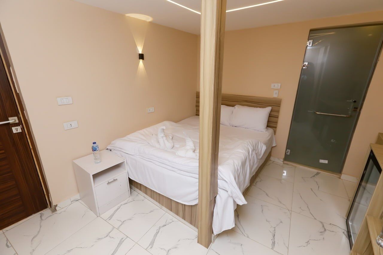 A hotel room with a bed, a nightstand, a wall-mounted light, a door, and a mirror.